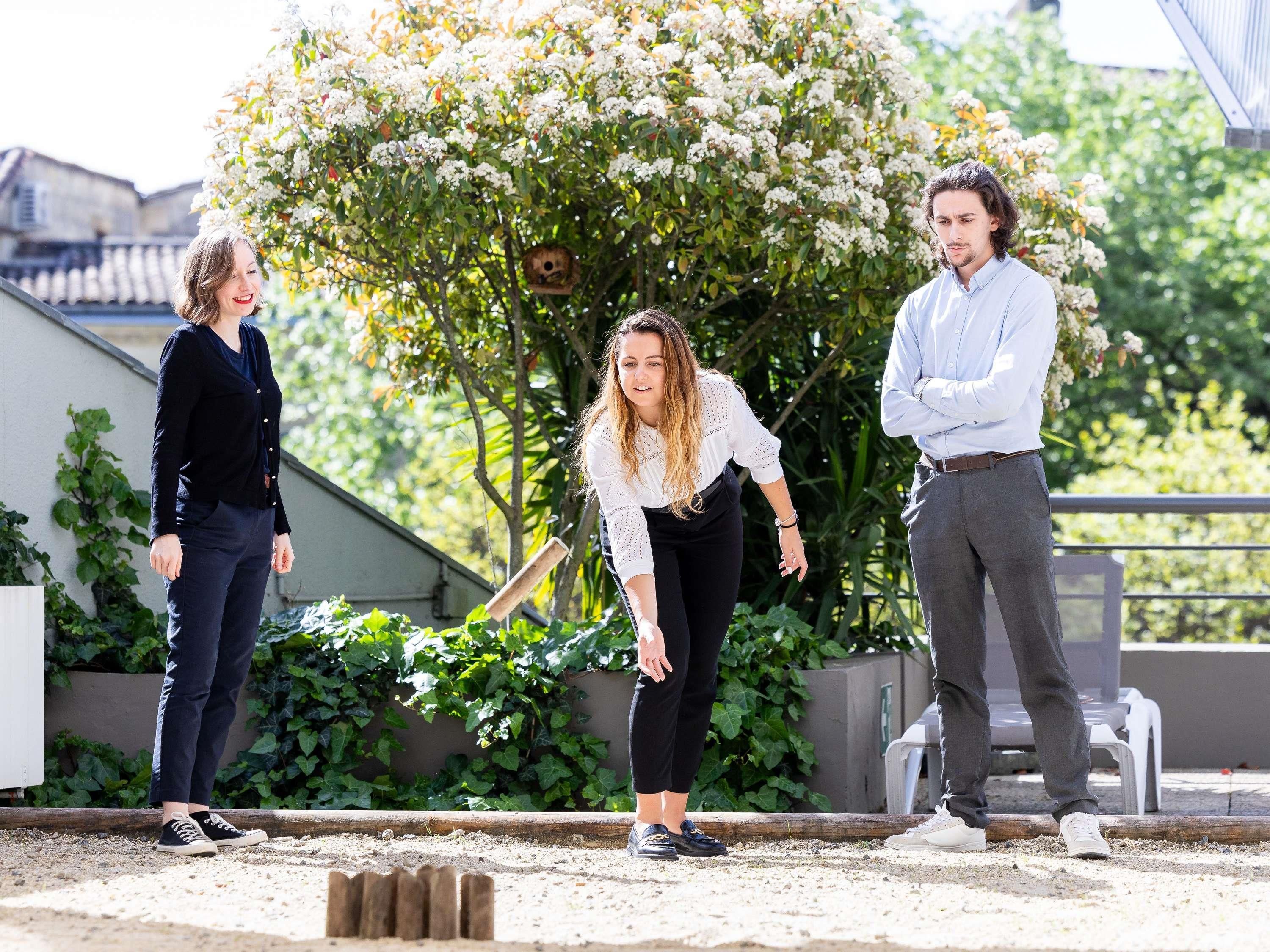 Three people standing outdoors with a tree and a building in the background.