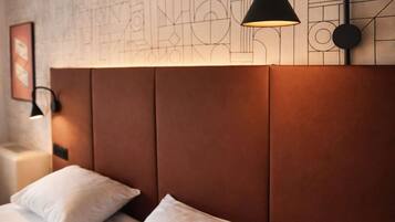 A hotel room with a bed, pillows, a nightstand, a lamp, and a wall with geometric patterns.