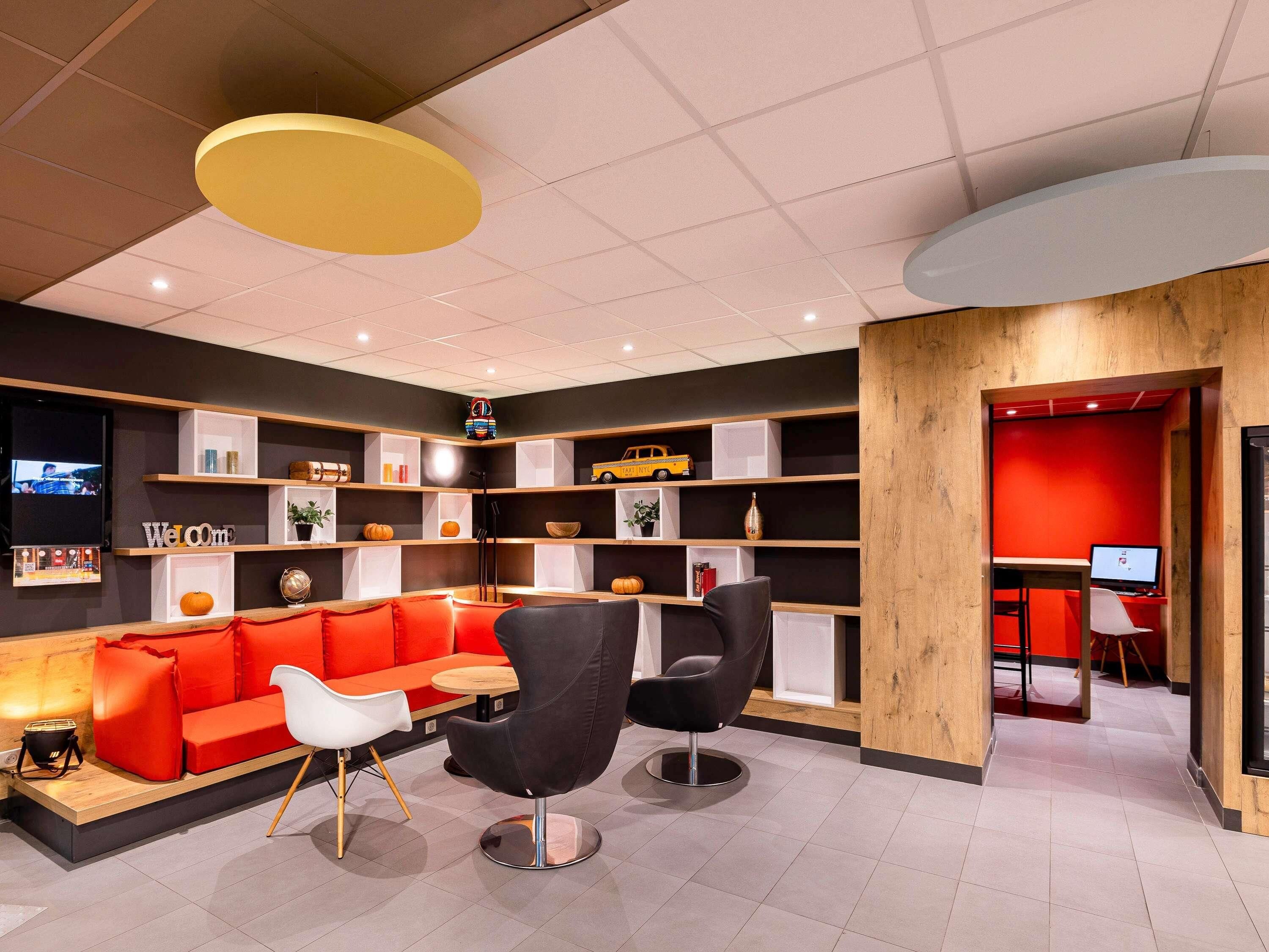 Ein modernes Interieur mit einem roten Sofa, schwarzen Stühlen, einem Holzbüro und einem Fernsehbildschirm.