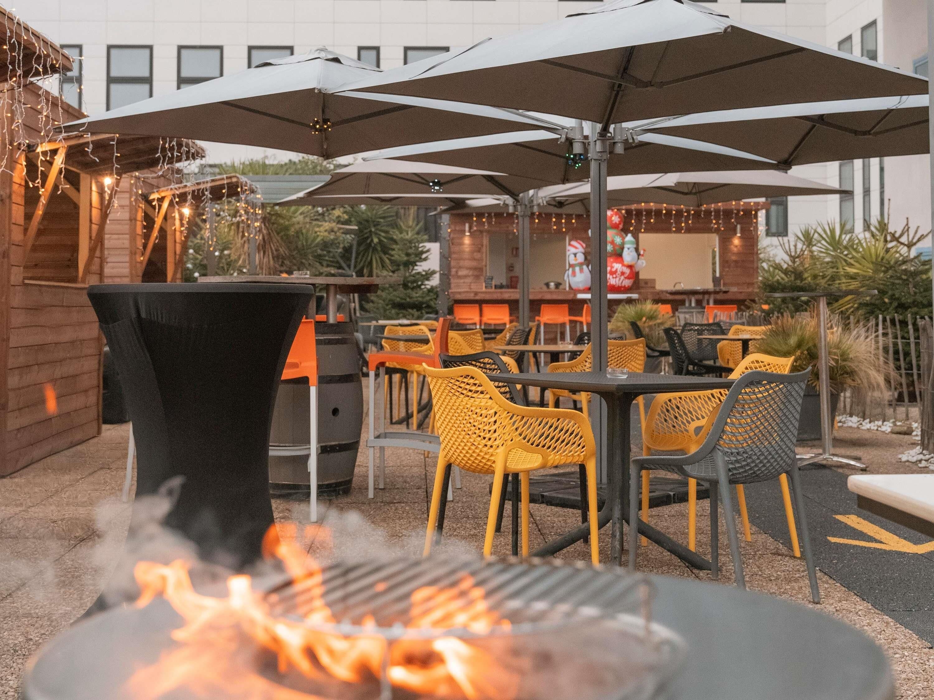 Una veranda esterna con tavoli e sedie, un barbecue e ombrelloni.