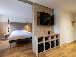 Una moderna camera d'albergo con un letto, una TV a parete, mensole integrate e un comodino con una lampada.