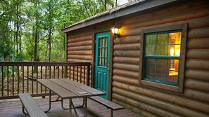 A wooden cabin with a green door, a window with a light inside, and a picnic table on a deck. - The Cabins at Disney's Fort Wilderness Resort (Lake Buena Vista)