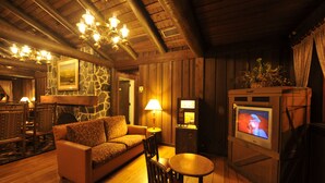 A cozy room with a stone wall, wooden furniture, a fireplace, a television, and a chandelier. - The Cabins at Disney's Fort Wilderness Resort (Lake Buena Vista)