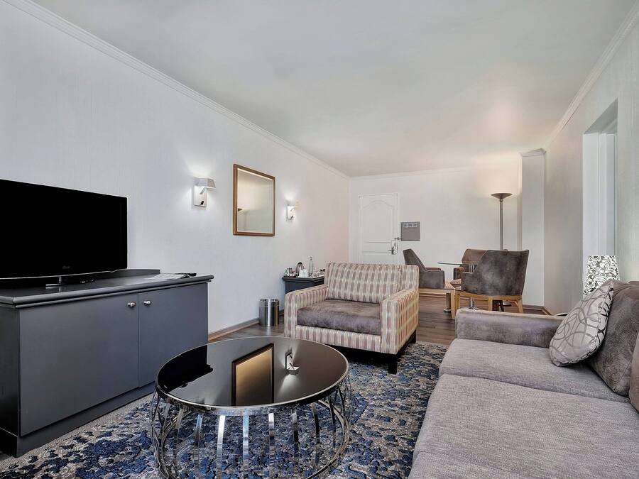 A modern living room with a flat-screen TV, grey sofa, striped armchair, and a round coffee table.