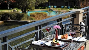 A dining table with a meal, wine glasses, and a vase with a flower, overlooking a pool and greenery. - Protea Hotel by Marriott Midrand (Midrand)