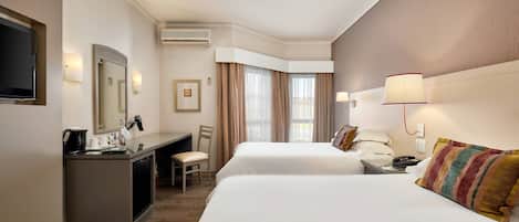 A hotel room with two beds, a desk, a chair, a TV, and a window with curtains.