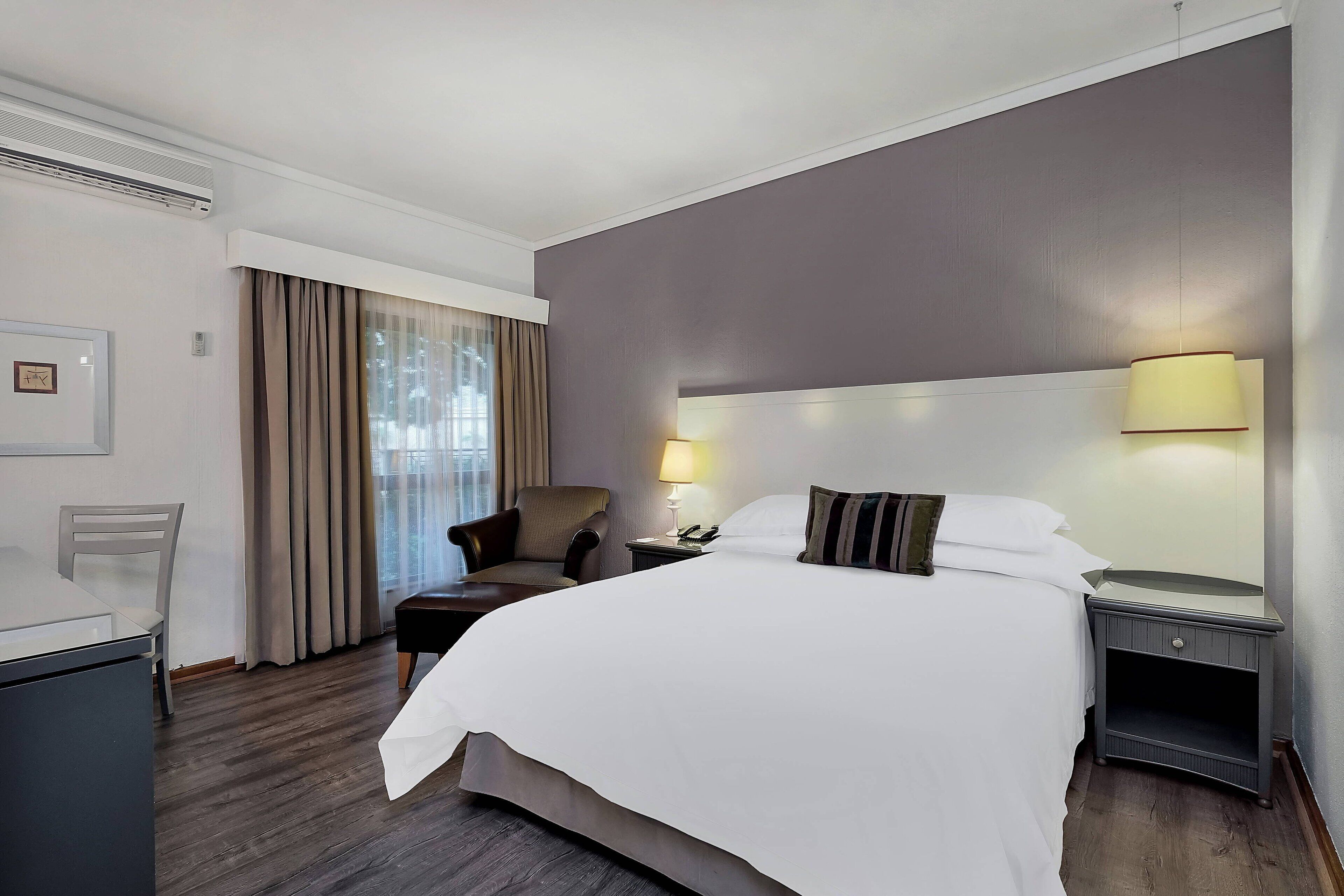Habitación de hotel con una cama grande, una silla, un escritorio y una mesita de noche con lámparas.