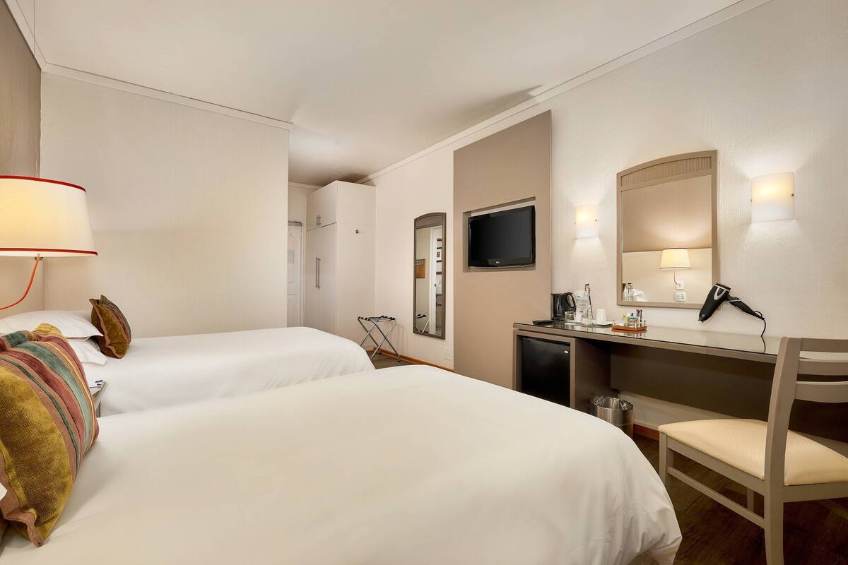 A hotel room with two beds, a desk with a chair, a TV, and a mirror.
