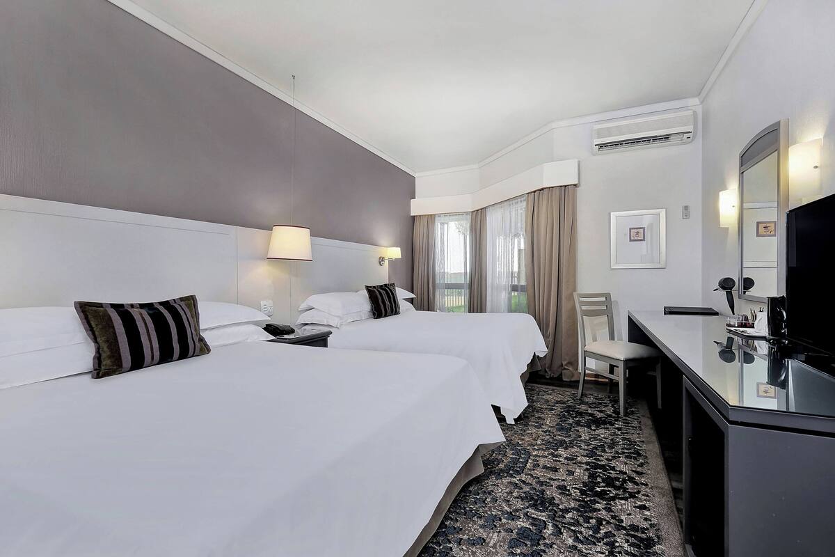 A hotel room with two beds, a desk, a chair, a TV, and a large mirror.