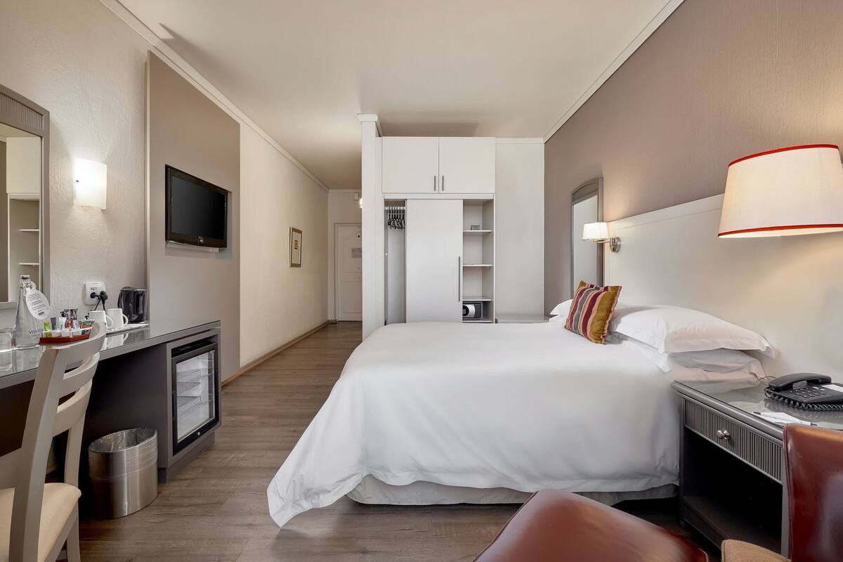 A hotel room with a bed, desk, chair, TV, and a wardrobe.