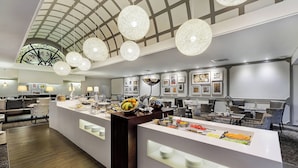 A modern hotel lobby with a central buffet area, seating arrangements, and a distinctive ceiling design. - Protea Hotel by Marriott Midrand (Midrand)