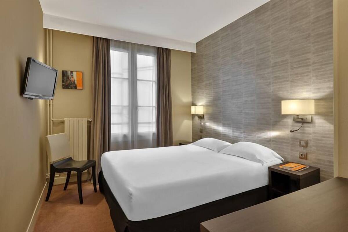 Een hotelkamer met een groot bed, een aan de muur bevestigde televisie, een bureau en twee bedlampjes.