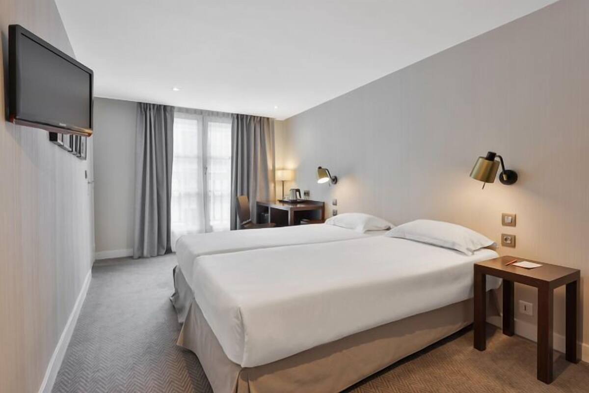 Een hotelkamer met twee bedden, een flatscreen televisie, een bureau met lamp en een kleine tafel met lamp.