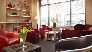 A modern lobby with red leather seating, a glass vase with flowers, and a city view through large windows. - Hôtel Londres et New York - Teritoria (Paris)