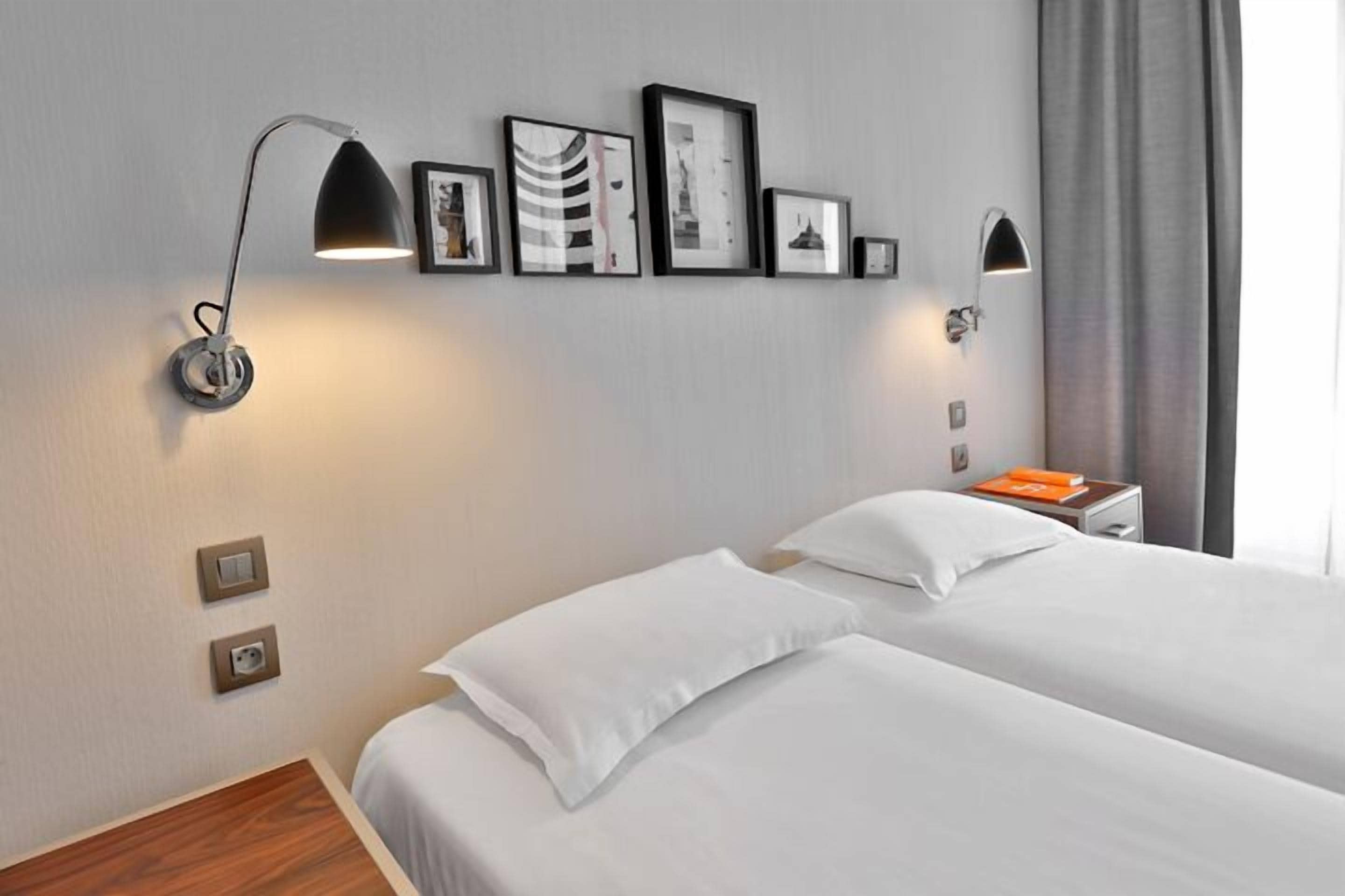 Habitación de hotel con dos camas, un escritorio empotrado, dos lámparas de pared y cuadros enmarcados en la pared.