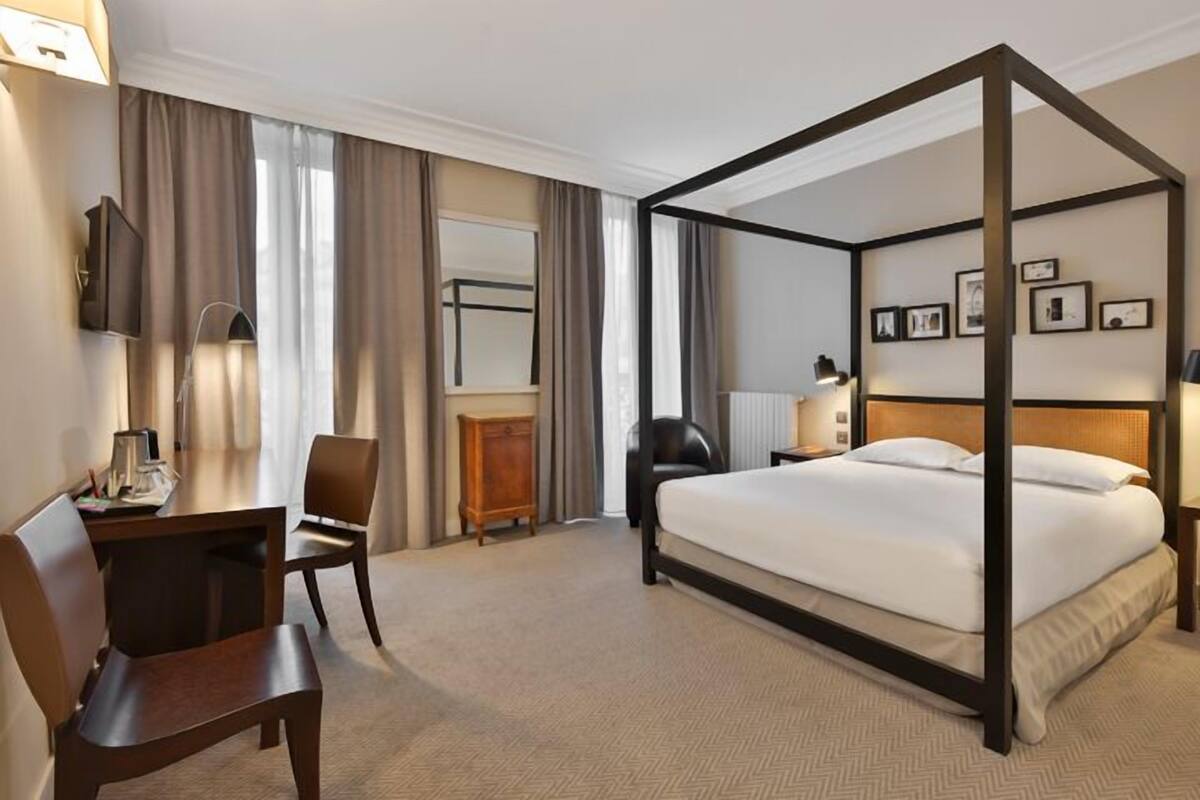 Een hemelbed met houten frame, een bureau met stoel, een televisie en een nachtkastje met lamp.