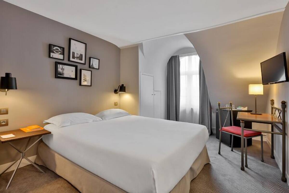 Een hotelkamer met een groot bed, een bureau met stoel, een televisie en ingelijste foto's aan de muur.