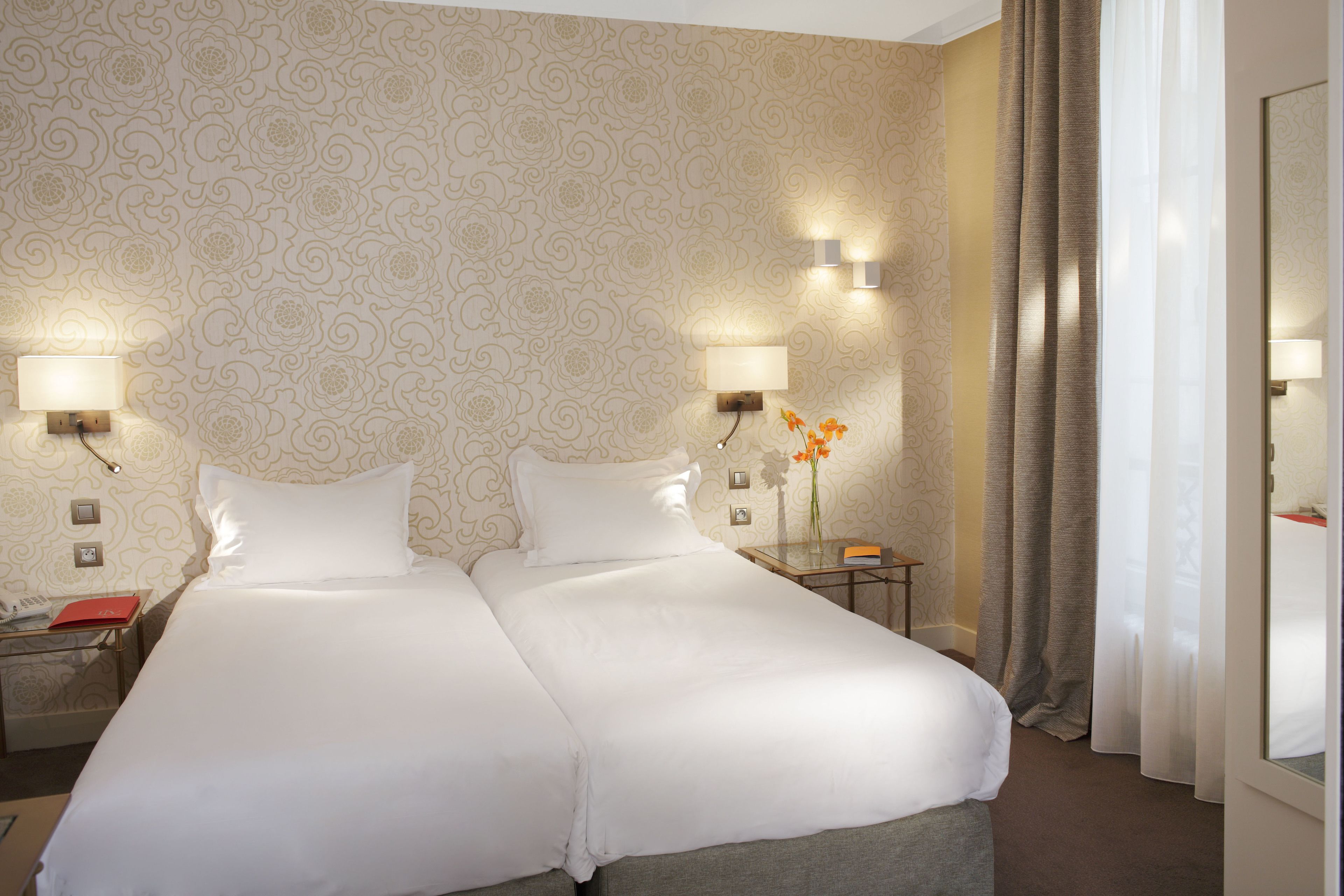 A double bed with white linens, two bedside tables with lamps, and a floral wallpaper pattern.