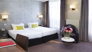 A hotel room with a double bed, two bedside tables, a chair, a small table with a vase of flowers, and a lamp on the wall. - Hôtel Londres et New York - Teritoria (Paris)