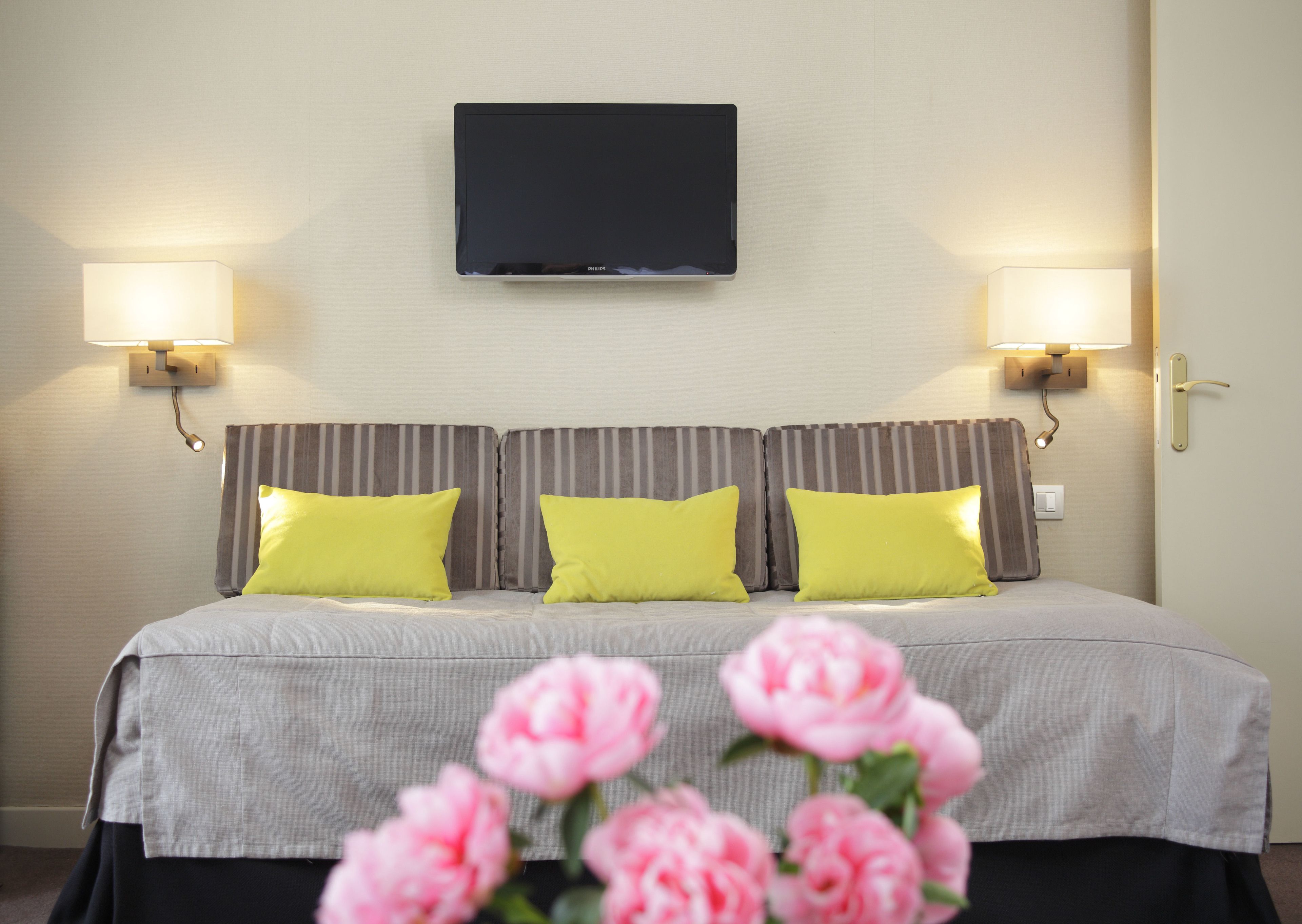 A hotel room with a bed, two bedside lamps, a flat-screen TV, and a floral arrangement.