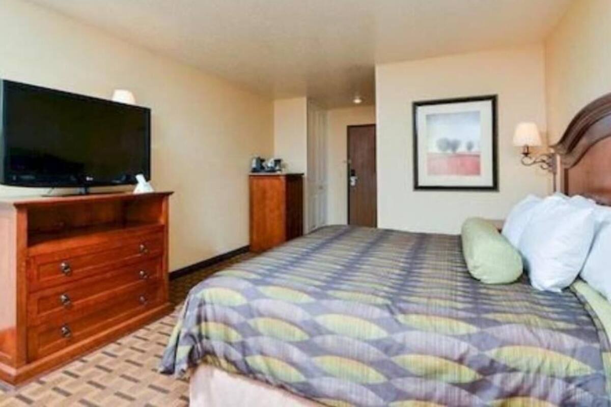 A hotel room with a bed, a television on a wooden dresser, a framed picture on the wall, and a door leading to another room.