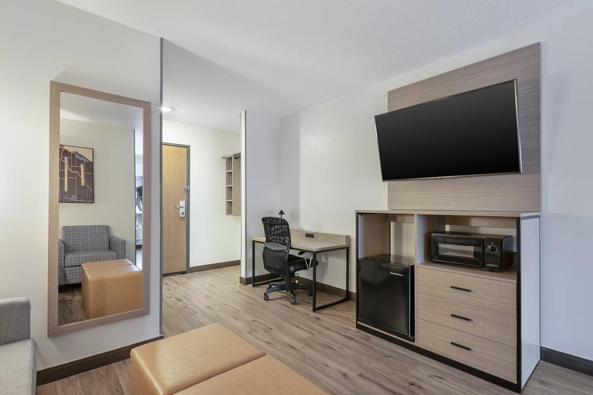 A modern room with a flat-screen TV, a desk, a chair, a microwave, and a sofa.