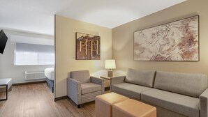 A modern hotel room with a sofa, armchair, bedside table, lamp, and artwork on the walls.