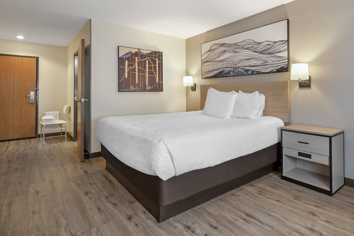 A hotel room with a large bed, bedside tables, a nightstand, a wall-mounted lamp, and a door.
