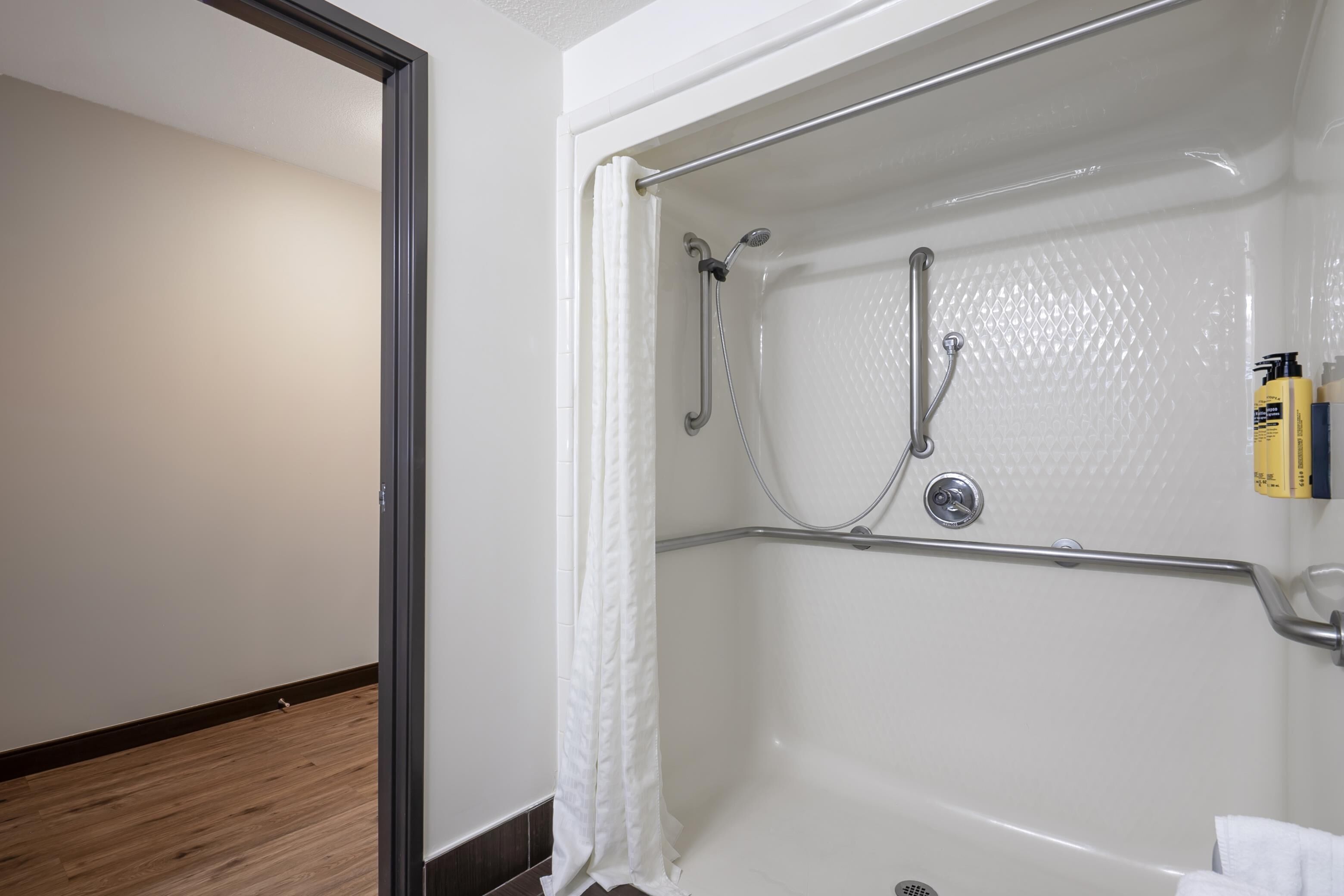 Un baño con bañera, ducha y barras de apoyo.