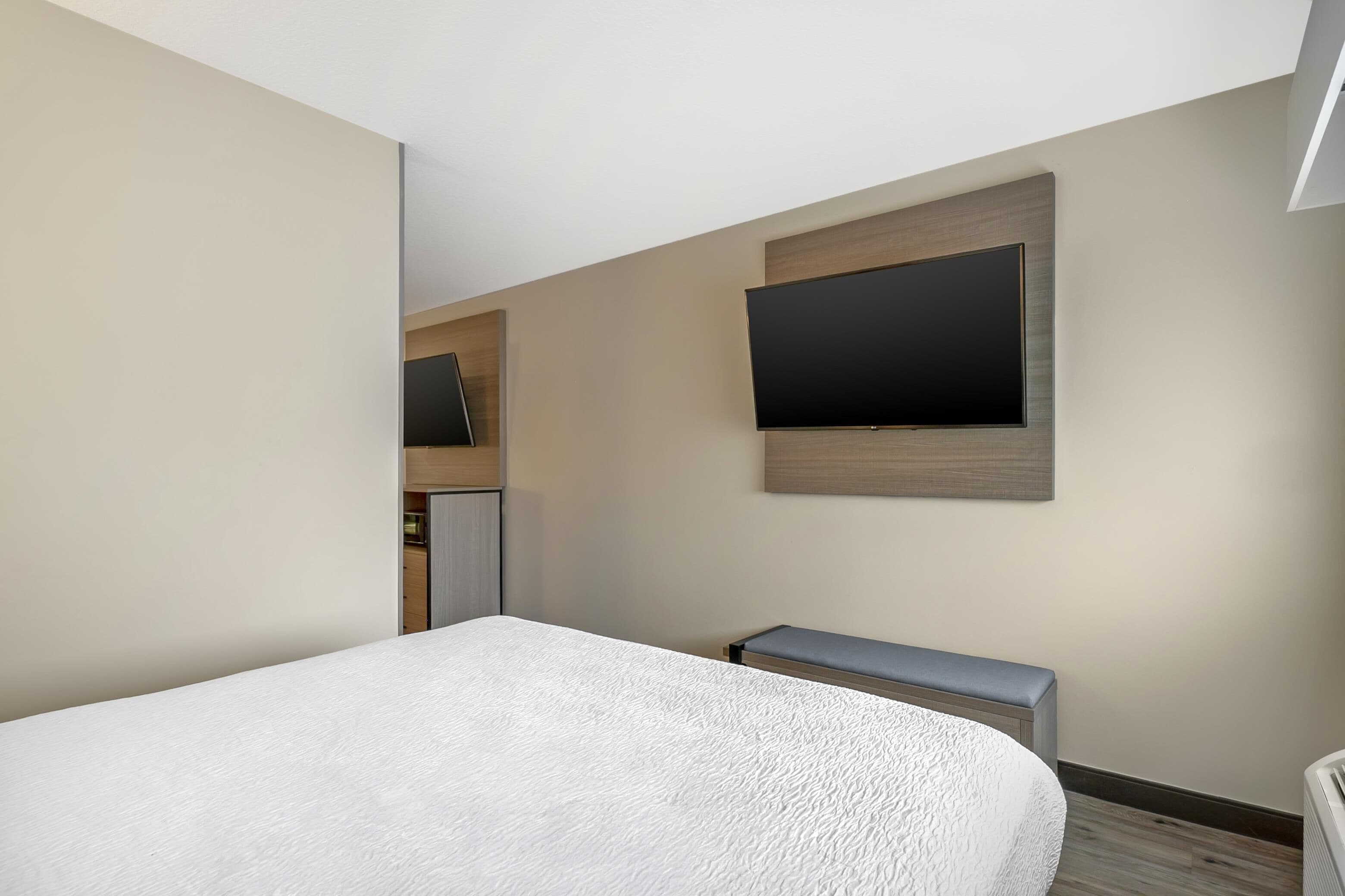 Een moderne hotelkamer met een groot bed, een flatscreen televisie aan de muur en een klein bankje.