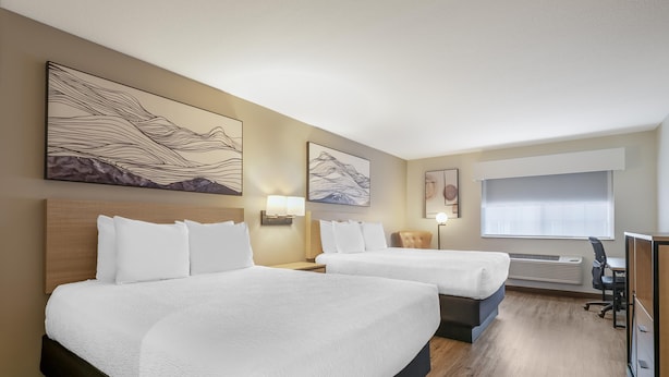 A hotel room with two beds, a desk, a chair, and artwork on the walls.