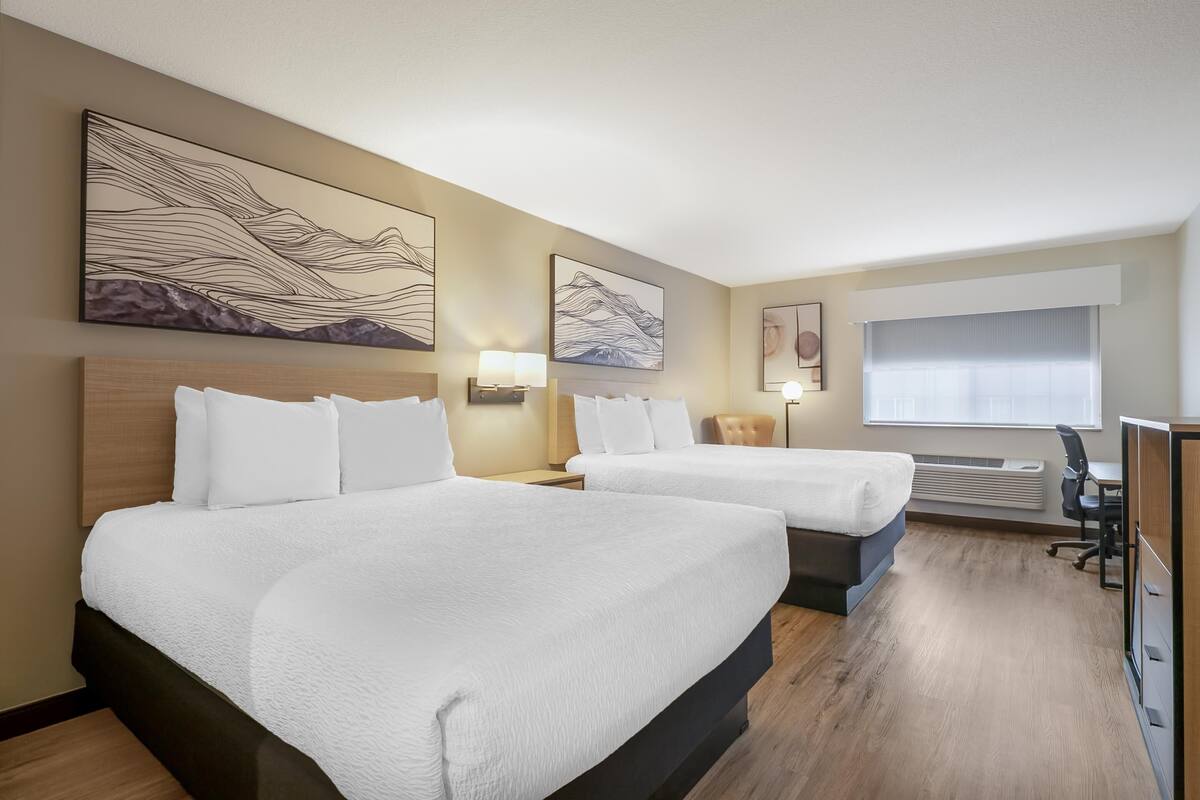 A hotel room with two beds, a desk, a chair, and artwork on the walls.