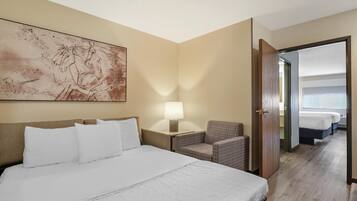 A hotel room with a large bed, a chair, a nightstand with a lamp, and a painting on the wall.