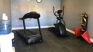 Ein Heim-Fitnessraum mit Laufband, Crosstrainer und Wasserspender.