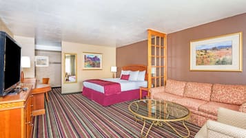 Una camera d'hotel con un letto, un divano, una TV, una scrivania e un tavolino in vetro.