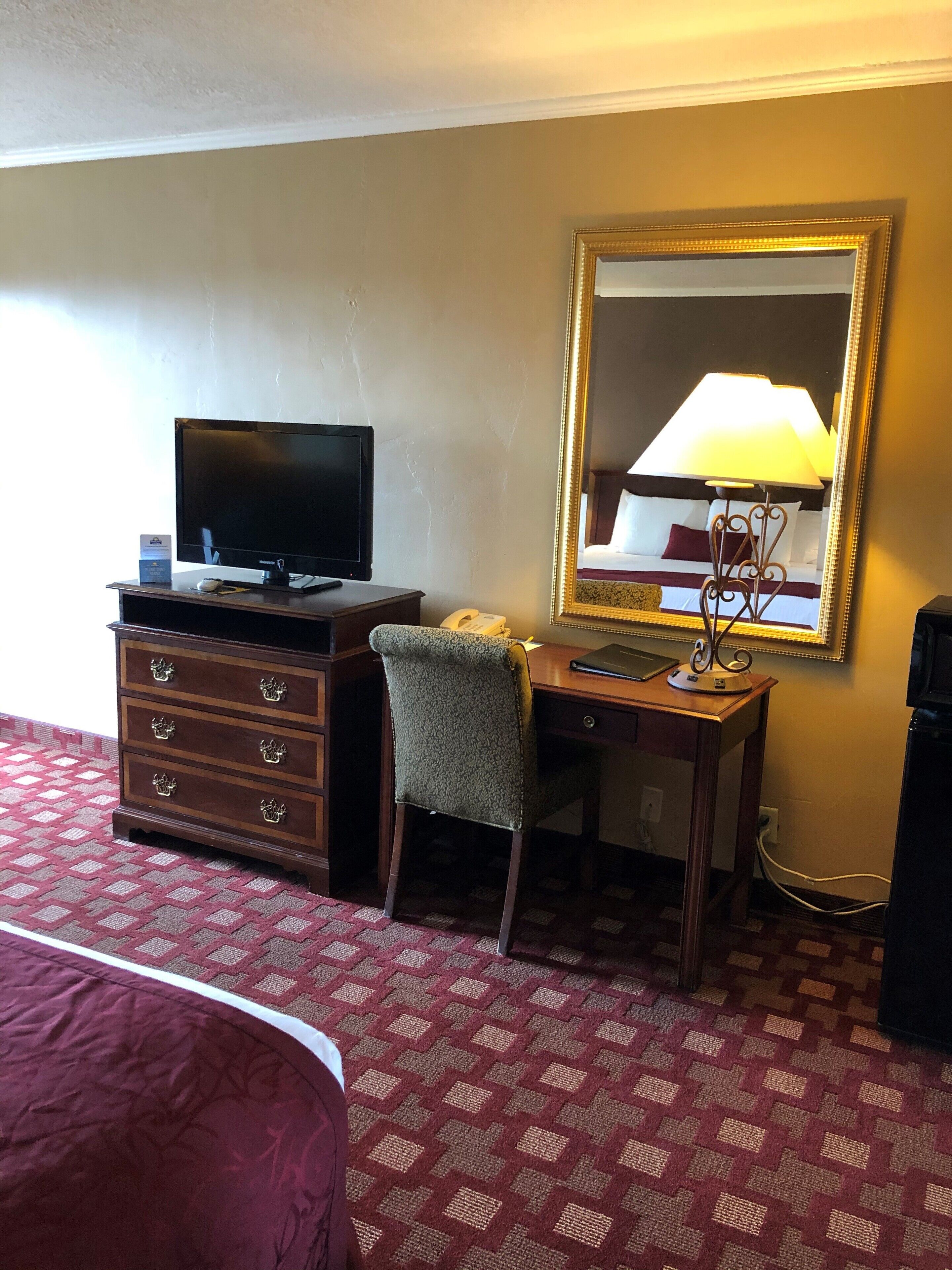 A hotel room with a bed, a desk with a computer, a telephone, and a mirror.