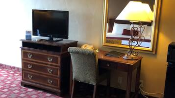 A hotel room with a bed, a desk with a computer, a telephone, and a mirror.