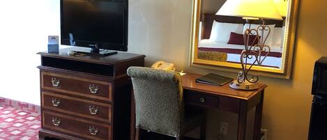 Habitación de hotel con cama, escritorio, computadora, teléfono y espejo.