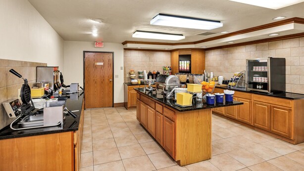A hotel kitchen with a self-service breakfast bar, a coffee machine, and various food dispensers. - Days Inn & Suites by Wyndham Logan (Logan)