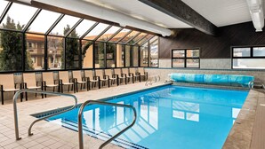 An indoor swimming pool with clear glass walls, a tiled floor, and a poolside seating area.