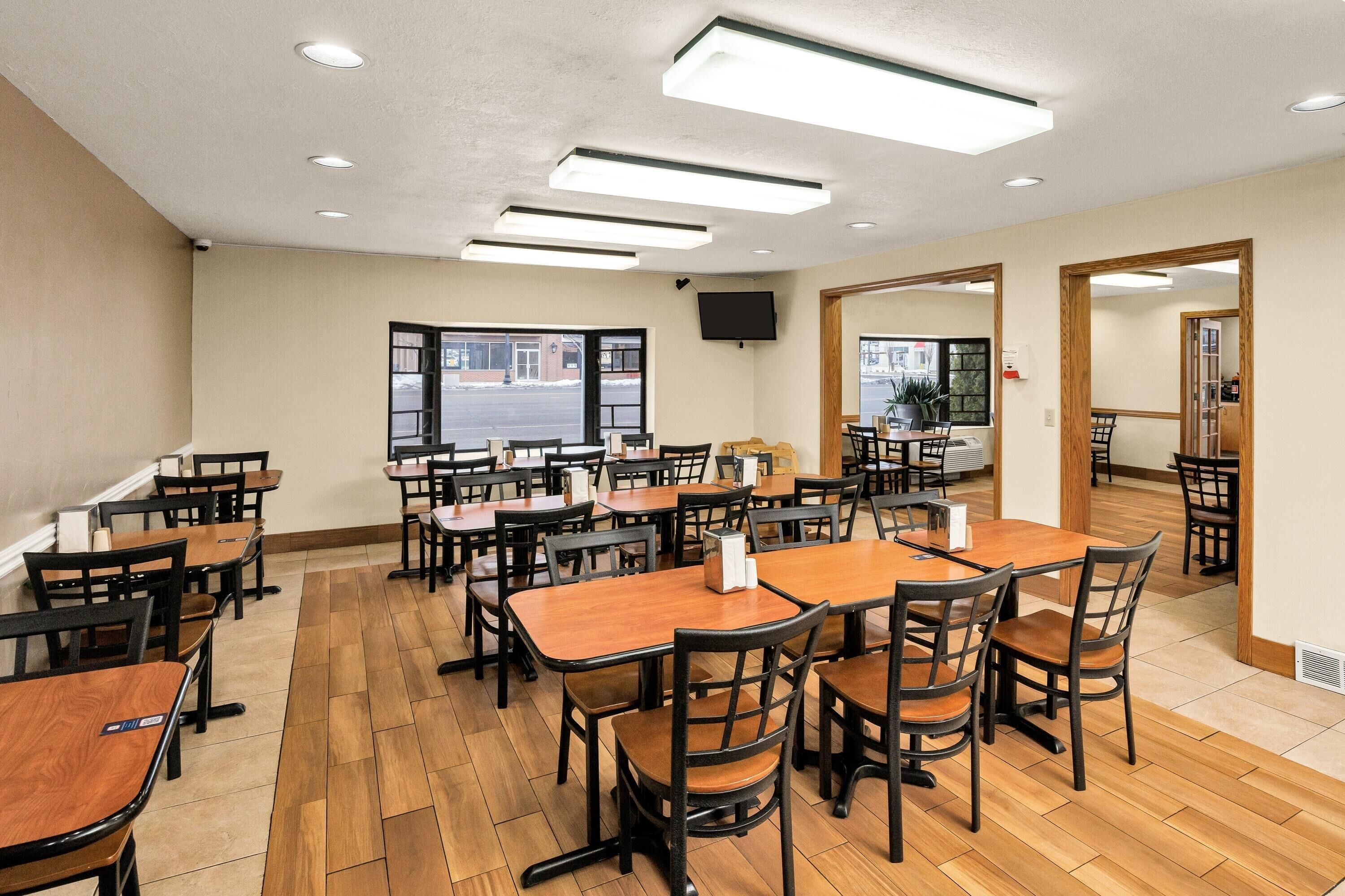 Un vaste espace dédié à la salle à manger, avec plusieurs tables et chaises, un téléviseur à écran plat fixé au mur et de grandes fenêtres offrant une vue sur l’extérieur.