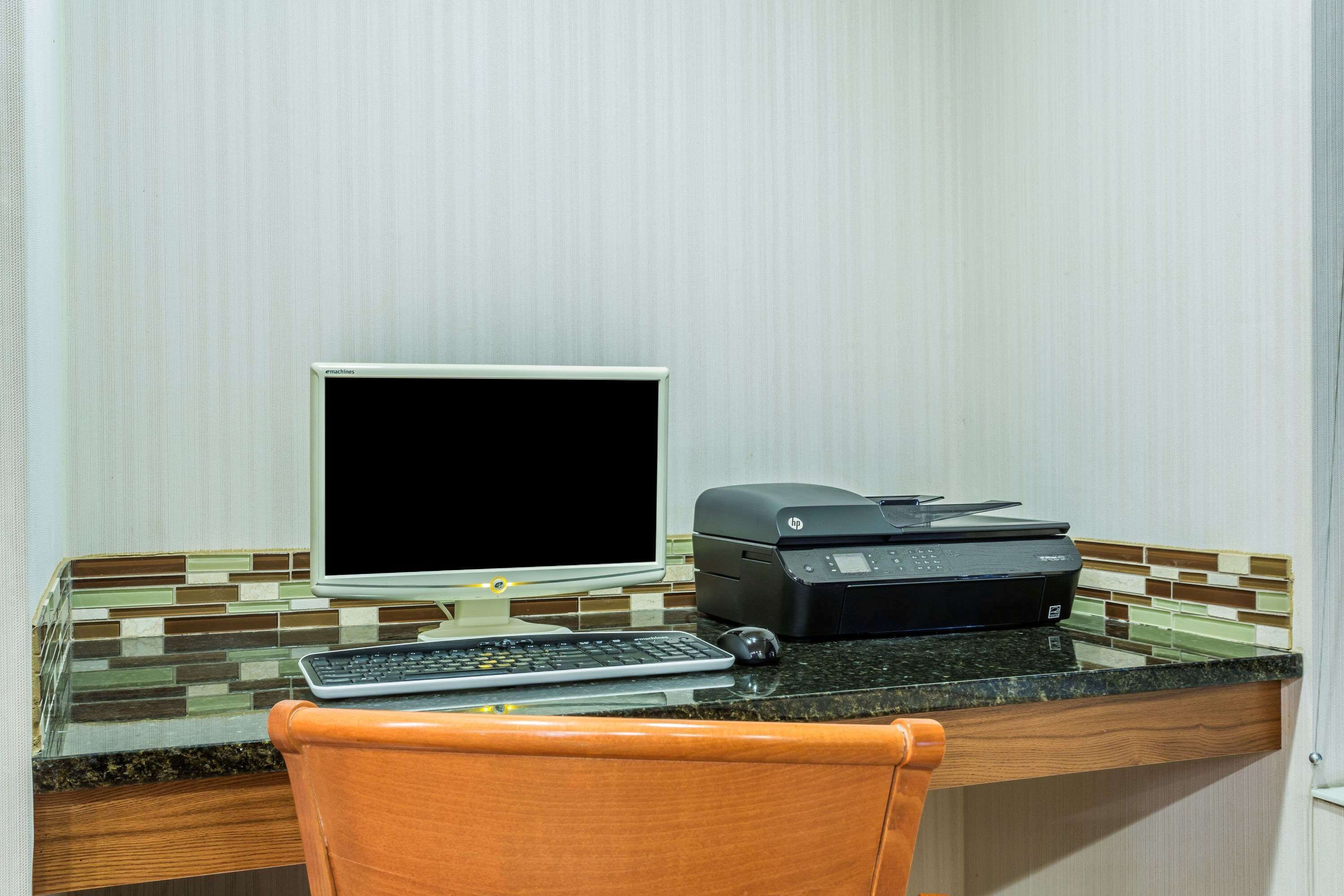 Uma área de trabalho com um computador de mesa, uma impressora e um teclado sobre um balcão.