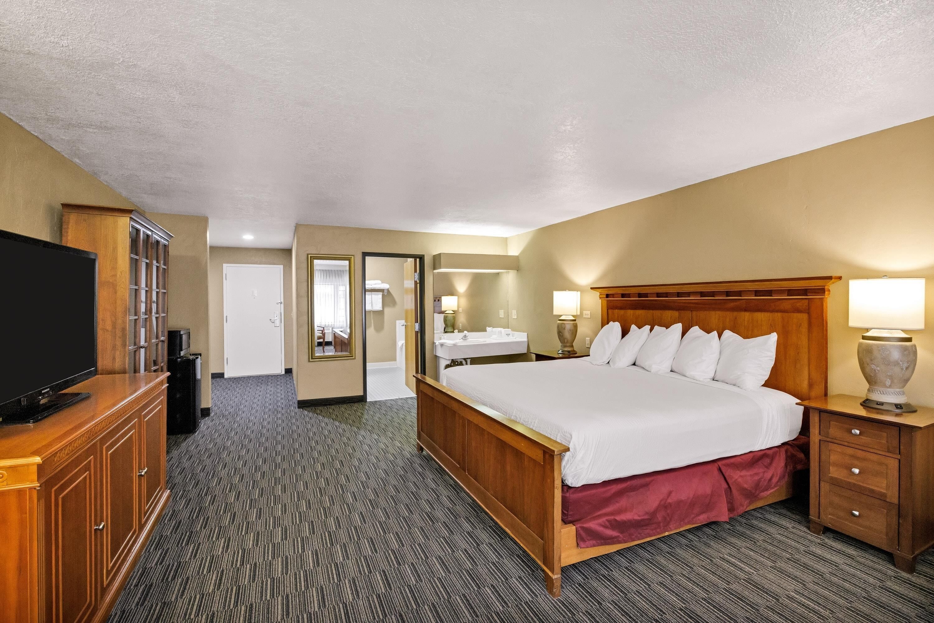 A hotel room with a bed, a television, a desk, and a bathroom visible through an open door.