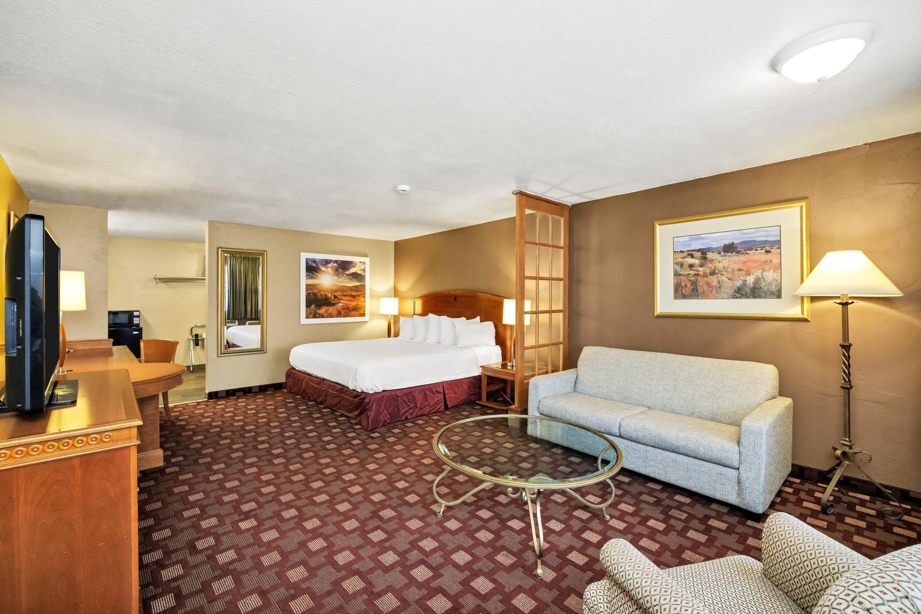 A hotel room with a bed, a sofa, a small table, a TV, a desk, and a mirror.