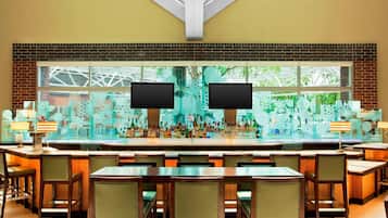 Zona de bar con varias opciones de asientos y un ventanal con vistas a la vegetación.