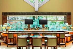 A bar area with multiple seating arrangements and a large window with a view of greenery. - Sheraton Indianapolis Hotel at Keystone Crossing (Indianapolis)