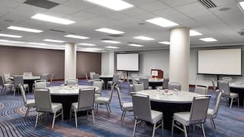 A conference room with round tables, chairs, and a projector screen.