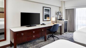 A hotel room with a large bed, a desk with a computer, a TV, and a small kitchenette.
