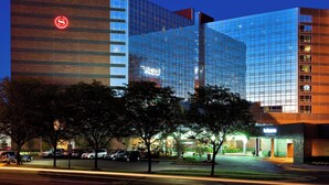 A modern hotel with a glass facade, a prominent red logo, and a well-lit entrance.