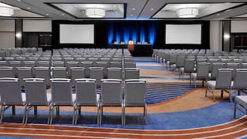 A conference room with rows of chairs, a stage with a podium, and a large screen.